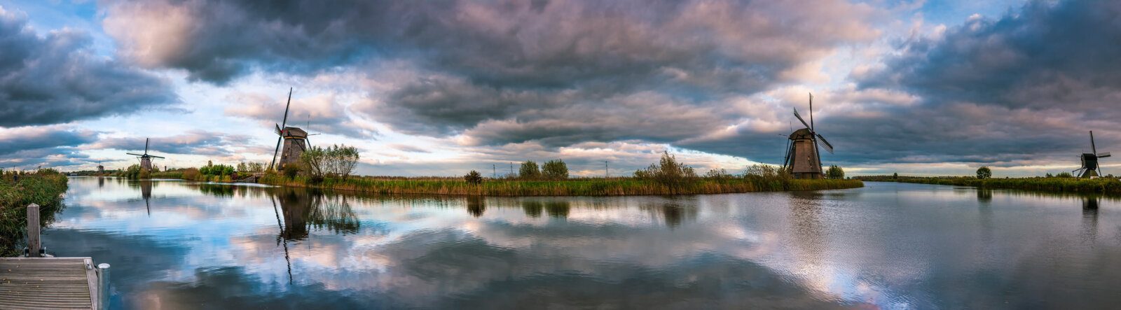 Panoramic view with threatening clouds during sunset, reflected in the water, at the windmills of Kinderdijk.