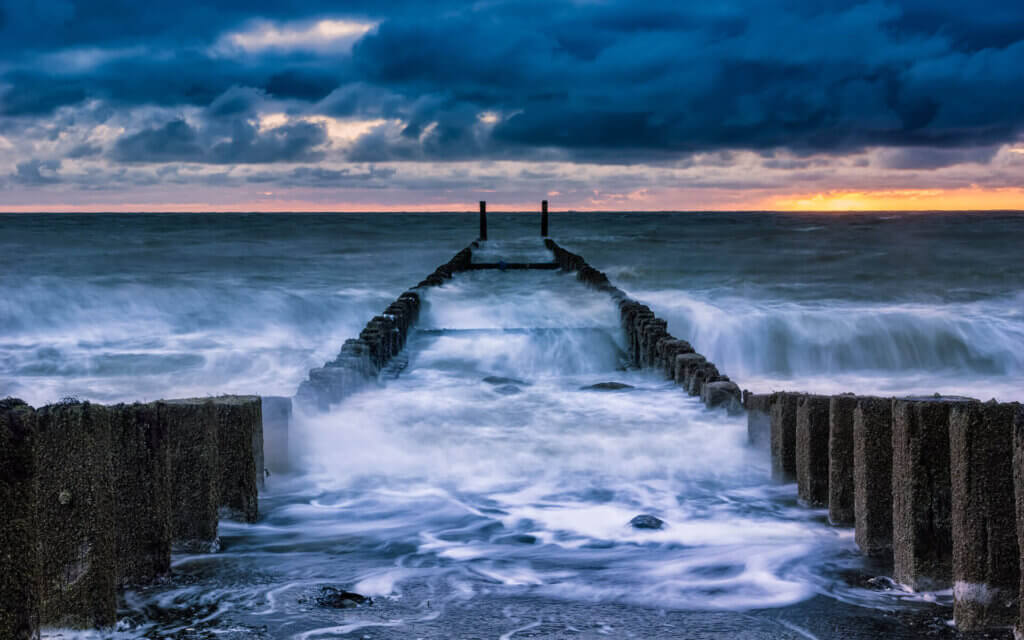 Rolling waves, during sunset, between the row of poles and against the dike of Westkapelle.