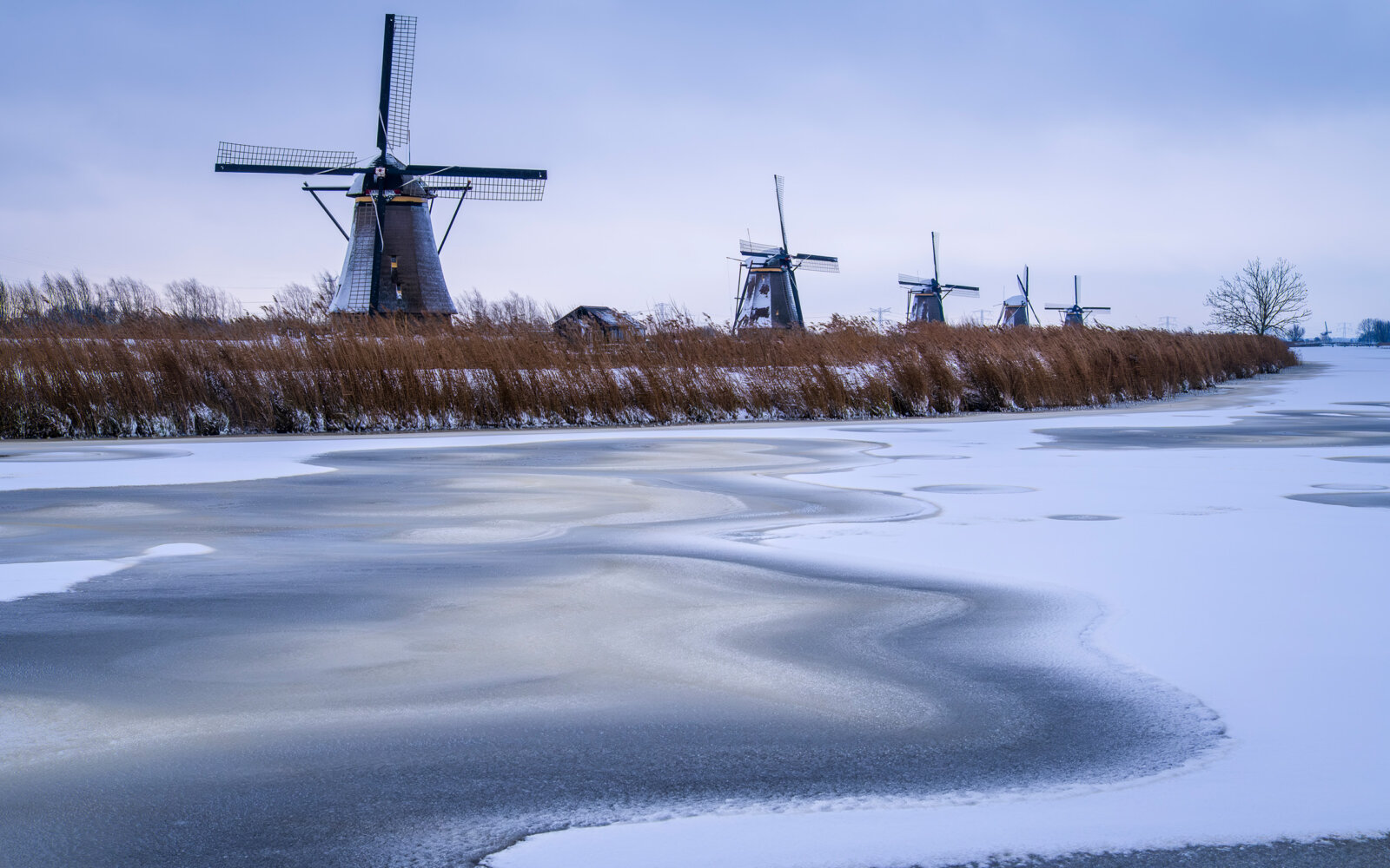 On a winter day at the frozen river between the Kinderdijk windmills with beautiful ice and snow patterns.