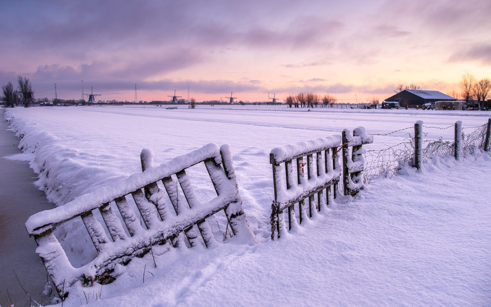 Winter polder landscape near Alblasserdam, snow and sunrise behind a wooden fence with view of the Kinderdijk windmills