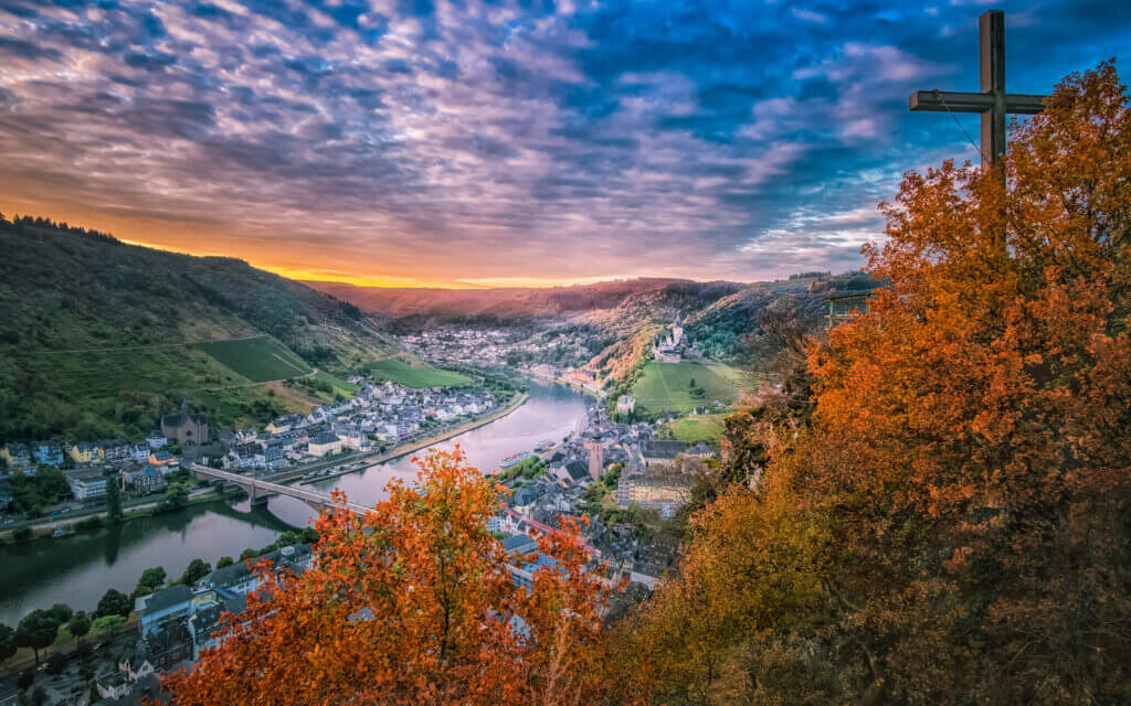 Early one morning, with a view of the city of Cochem from the Pinnerkreuz observation platform. We see Cochem Castle, St. Martin's Church, the Skagerak Bridge, and the Moselle River at sunrise.