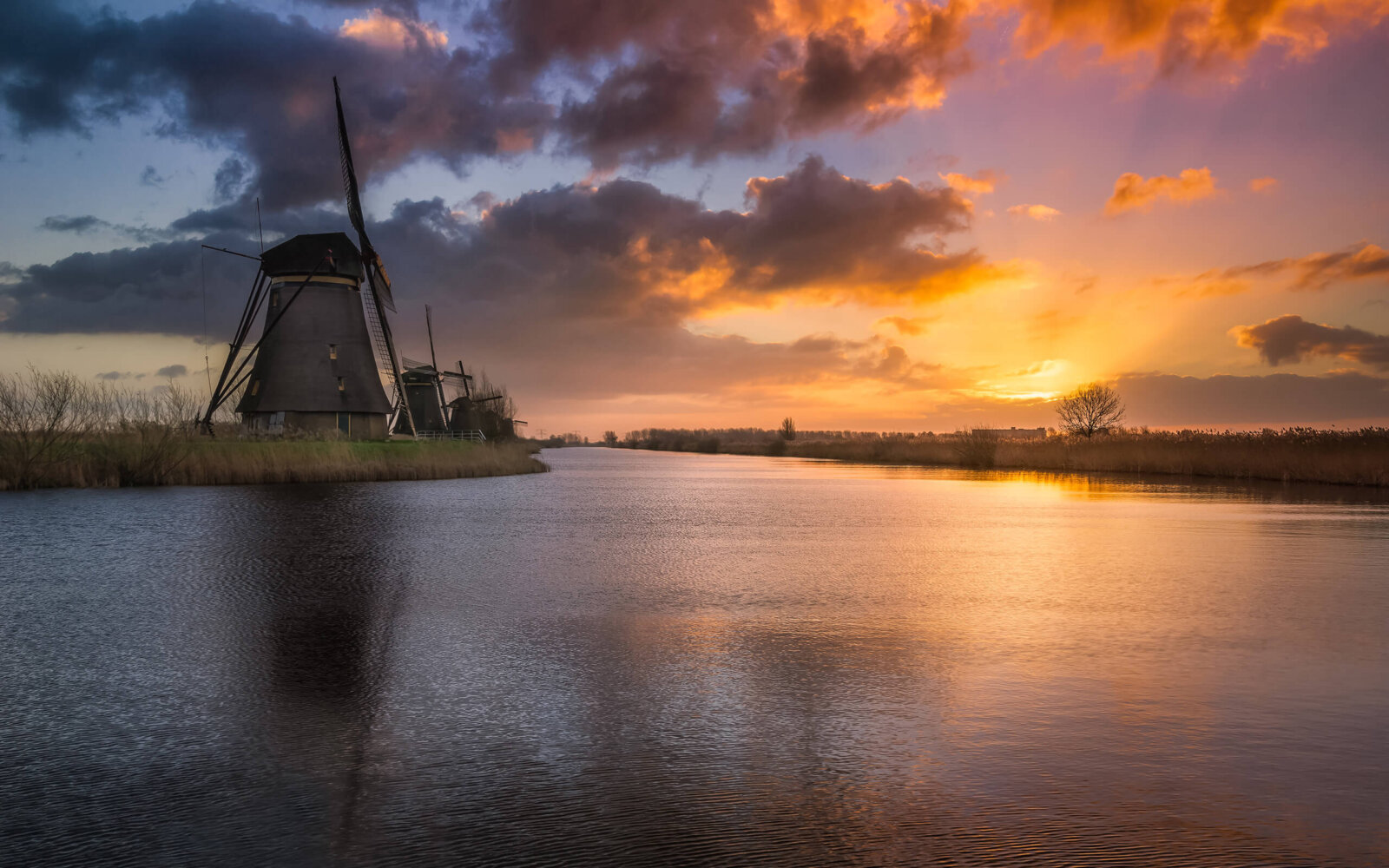 Kinderdijk A calm, peaceful sunrise at the windmills of Kinderdijk. The sun shines its rays upwards and colors the cloud cover.